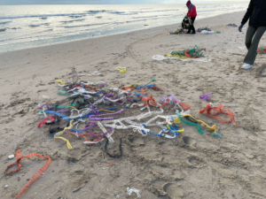 Multicoloured mussels socks lay strewn on a beach as people clean up.